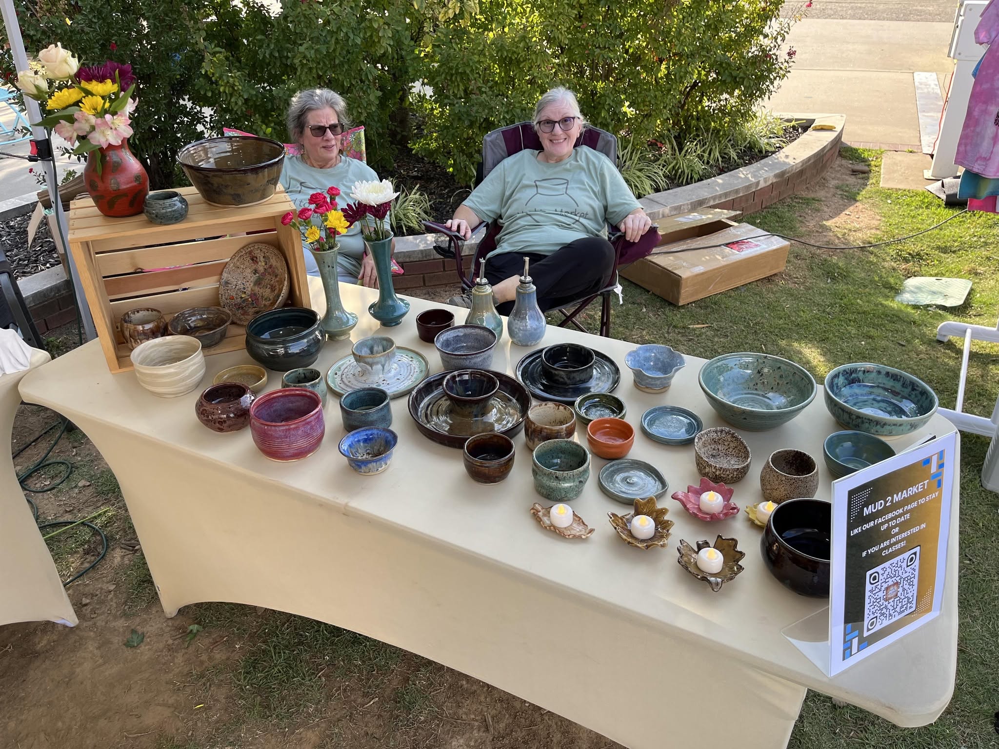 Two Mud to Market potters seated behind a table of handmade ceramics at an outdoor market